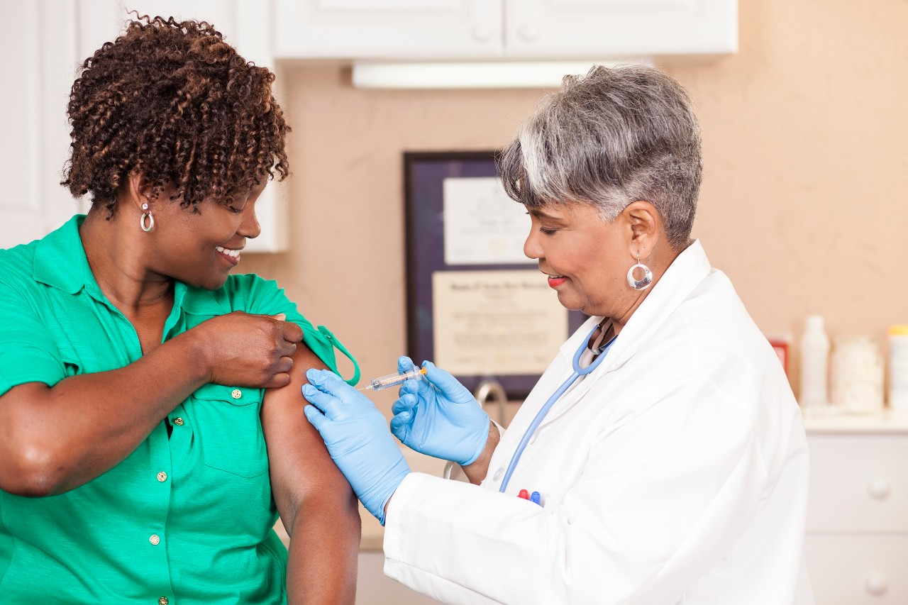 Senior adult doctor or nurse gives flu vaccine to African descent, mid-adult patient at a local medical clinic, hospital, or doctor's office.  NOTE:  This is a studio shot and not an actual medical clinic.