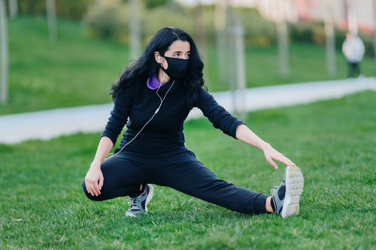 Young woman stretching on grass in public park