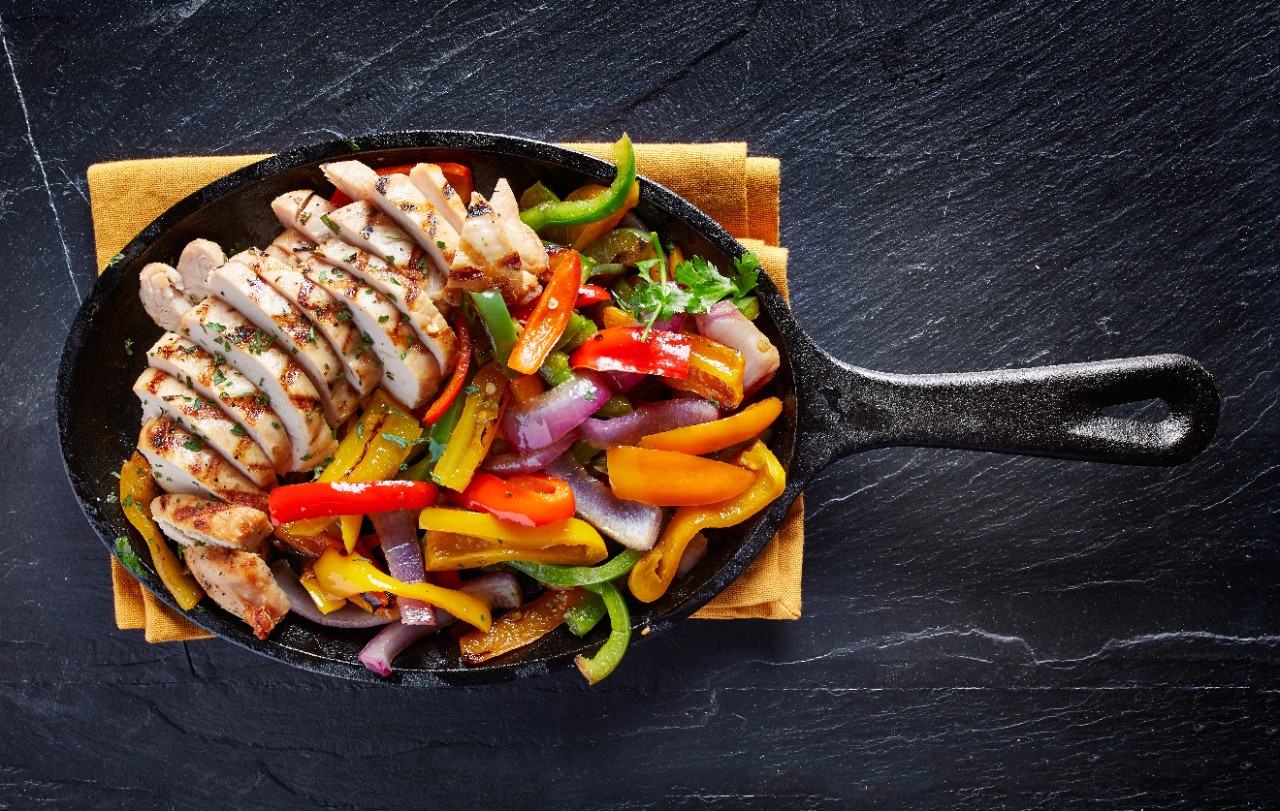 mexican grilled chicken fajitas in iron skillet shot from overhead on dark slate
