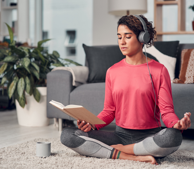 Full length shot of an attractive young woman sitting and listening to music while reading in her living room