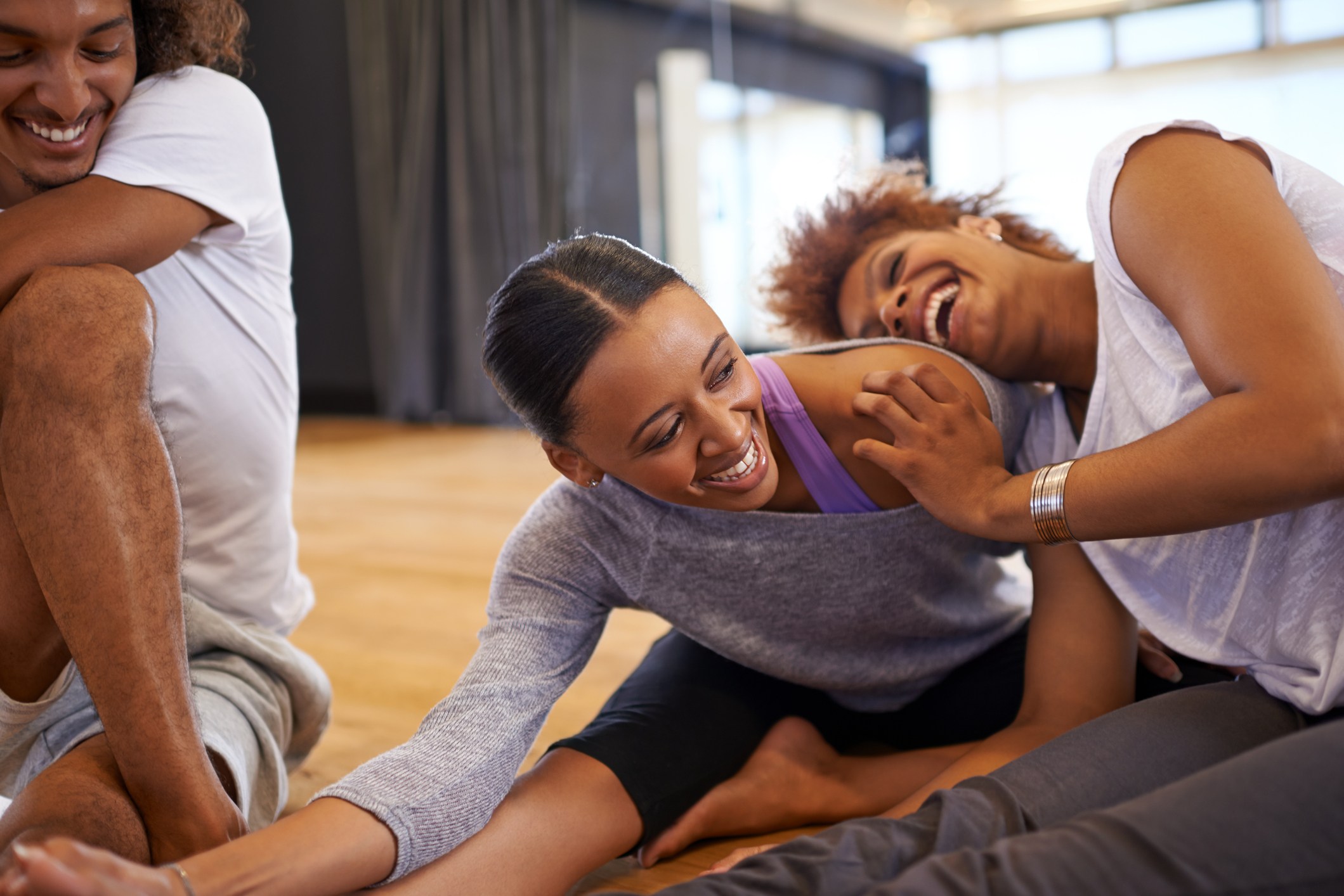 Shot of three happy young women dancers stretching on the floor