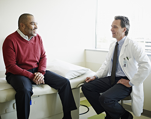 Mature male patient sitting on exam table in discussion with doctor in exam room