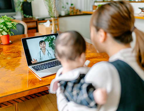 A mother with her baby is video calling a doctor on a laptop from home.