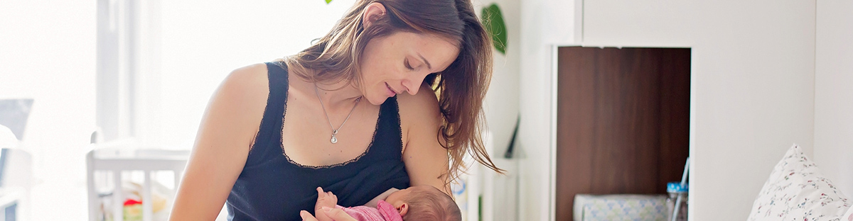 Young mother breastfeeds her baby, holding him in her arms and smiling from happiness