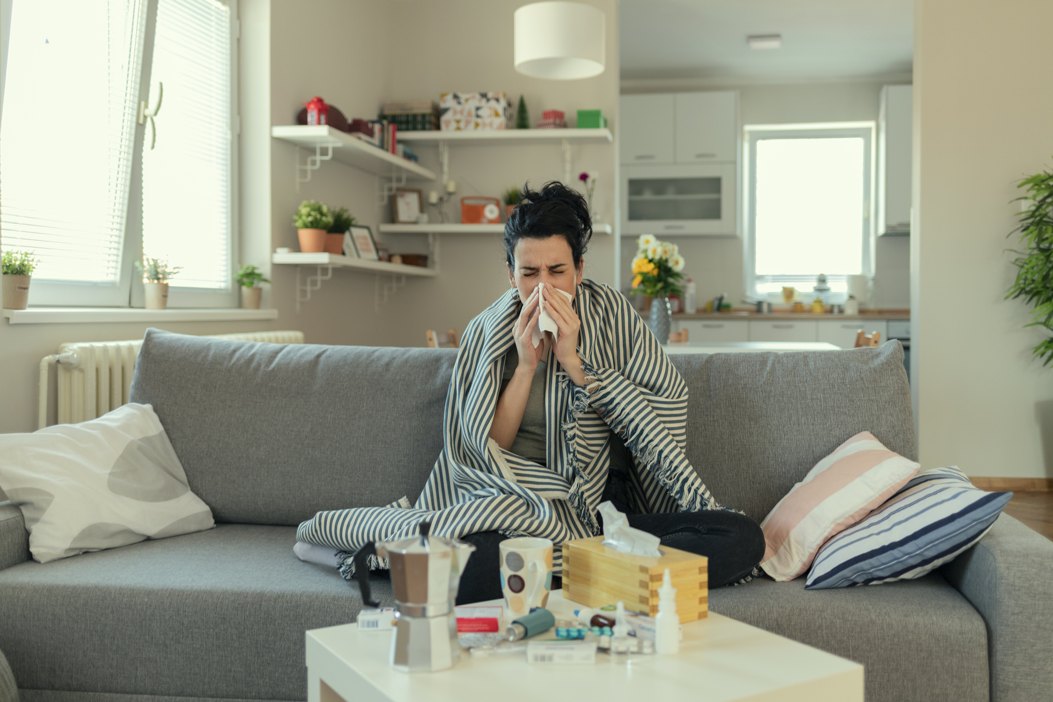 Sick Woman Covered With a Blanket Lying in Bed With High Fever and a Flu, Resting at Living Room. She Is Exhausted and Suffering From Flu. Sick Woman With Runny Nose Lying in Bed. Girl Suffering From Cold Lying in Bed With Tissue Blowing Her Nose While Sitting on the Sofa