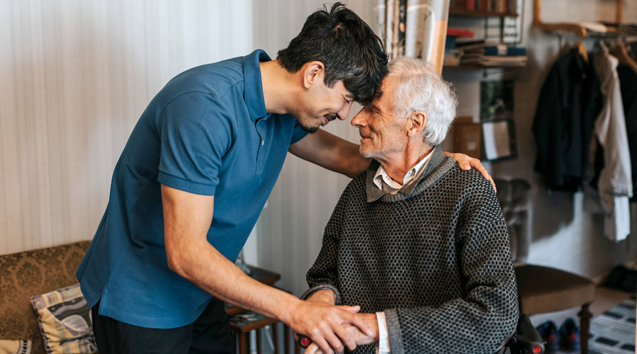 A male caregiver holding the hand pf an elderly man, offering support and comfort.