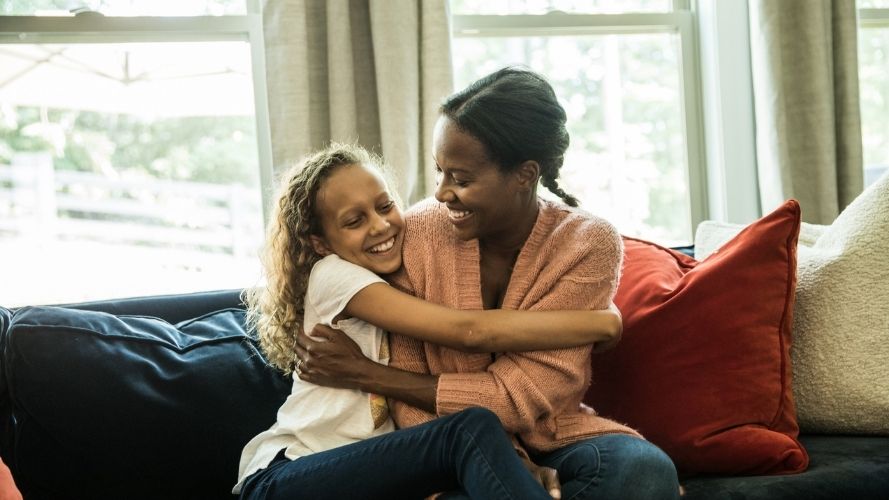 Black mother and daughter embracing on sofa