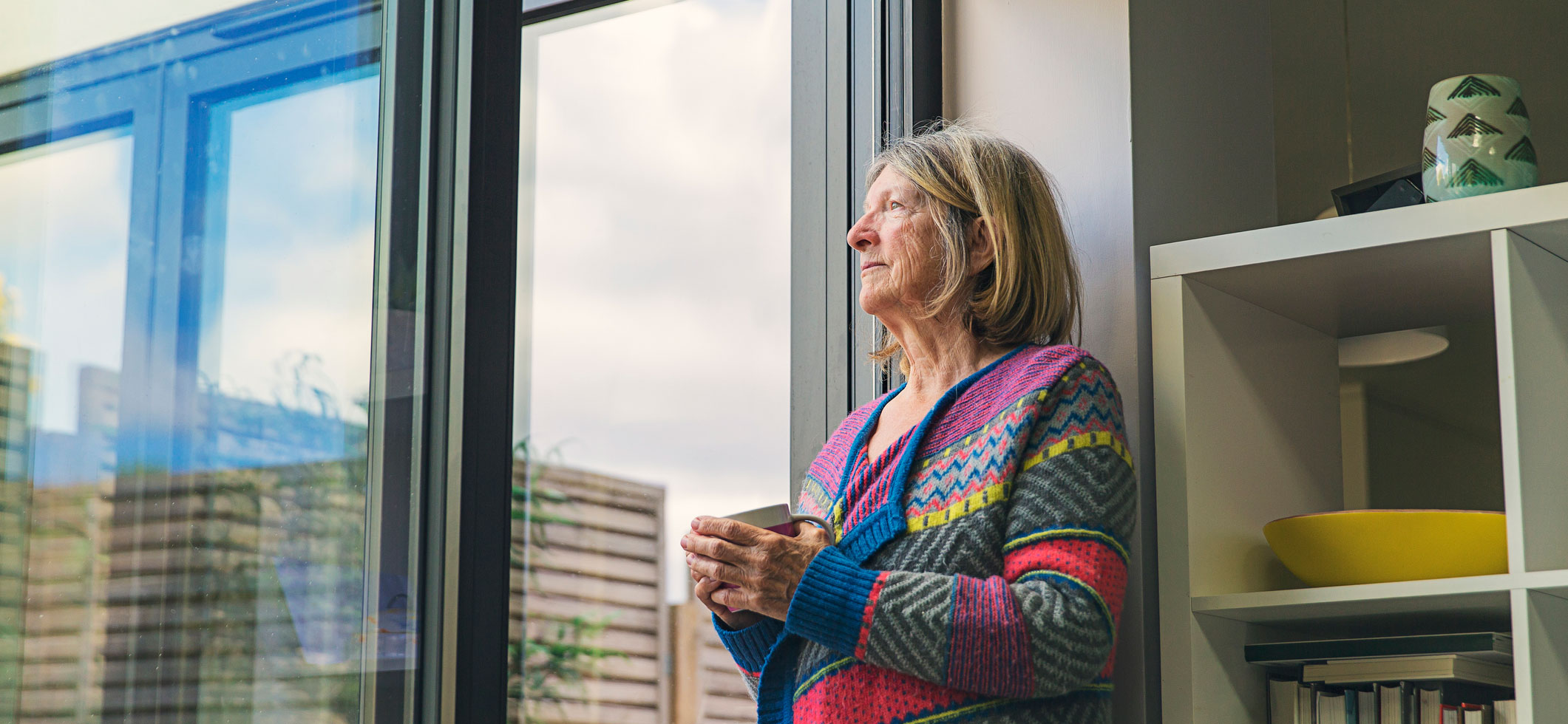 Elderly woman looking outside the windows of New York City while drinking coffee.