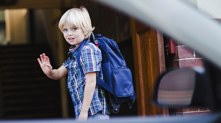 young boy with backpack waving goodbye before school and smiling