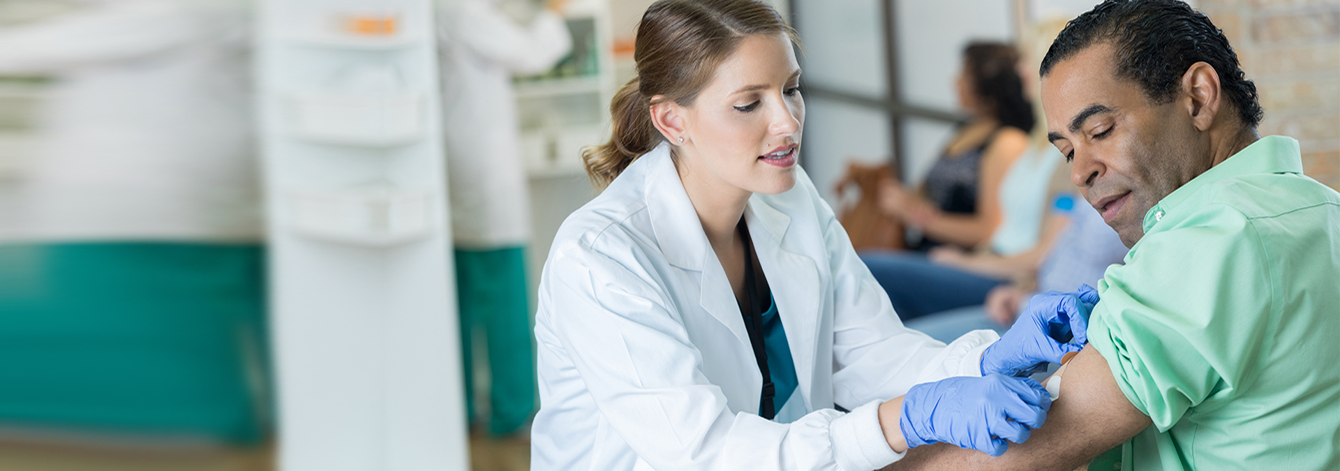 Confident mid adult Caucasian female healthcare professional gently places a bandage on a mature male patient's arm. The patient received a flu or other preventative vaccine.