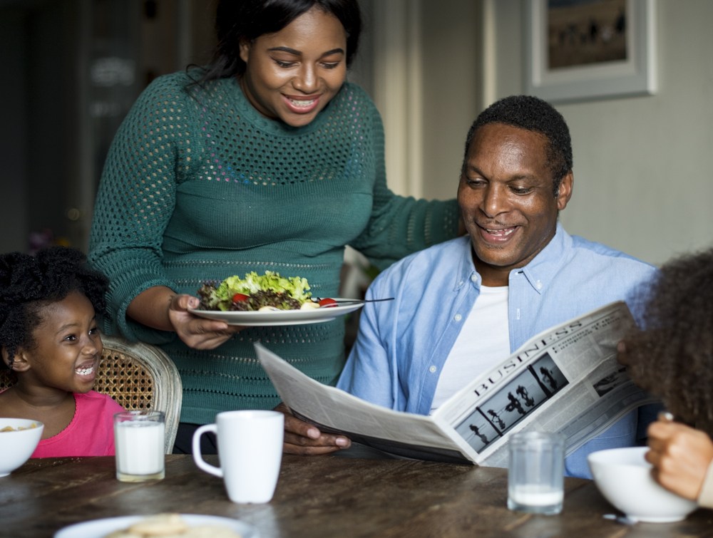 Woman serving husband salad as he reads paper.