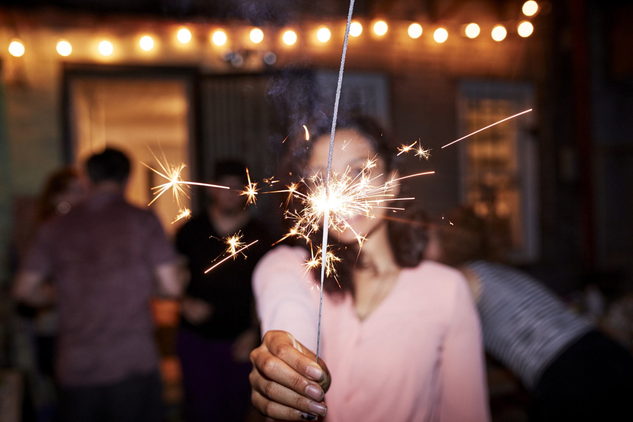 Smiling Mixed Race woman holding burning sparkler at backyard party