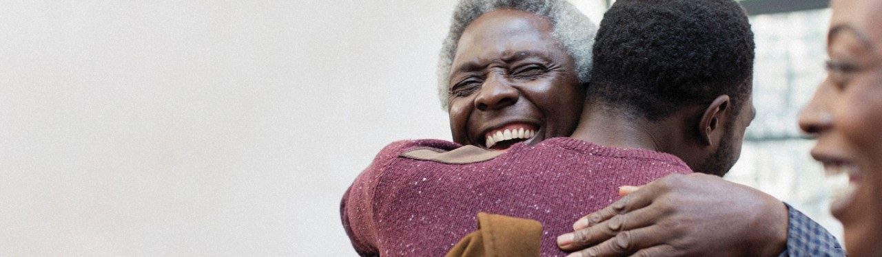 Man with gray hair embracing other man, smiling.