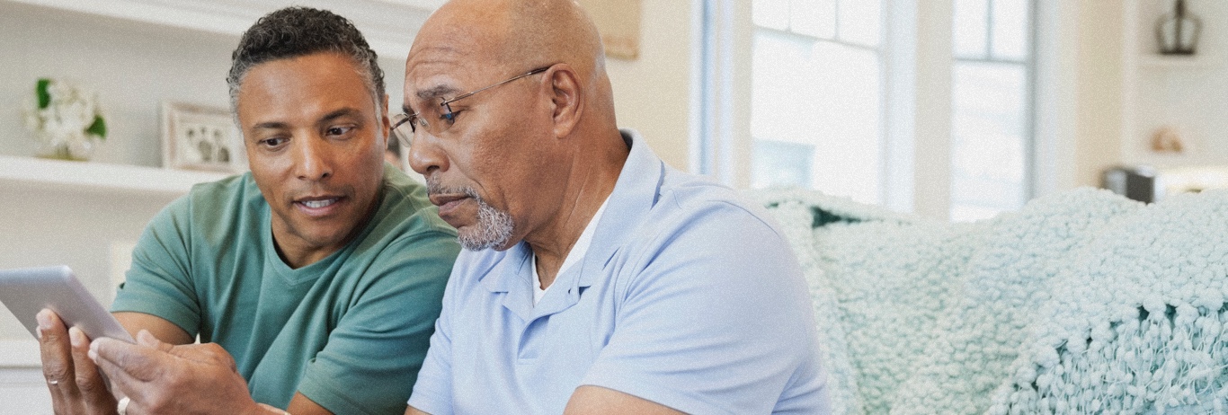 Man sitting on couch with father looking at a tablet PC.