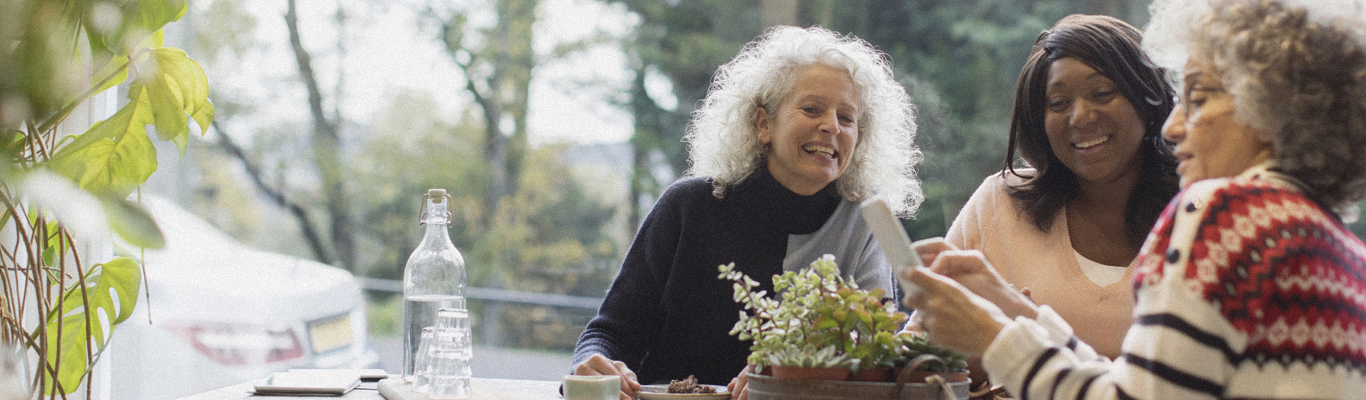 Three older woman laughing and looking at phone.