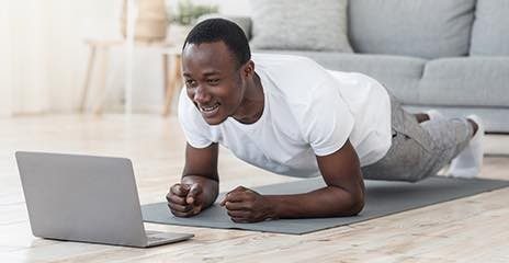 Male is doing plank in front of his laptop
