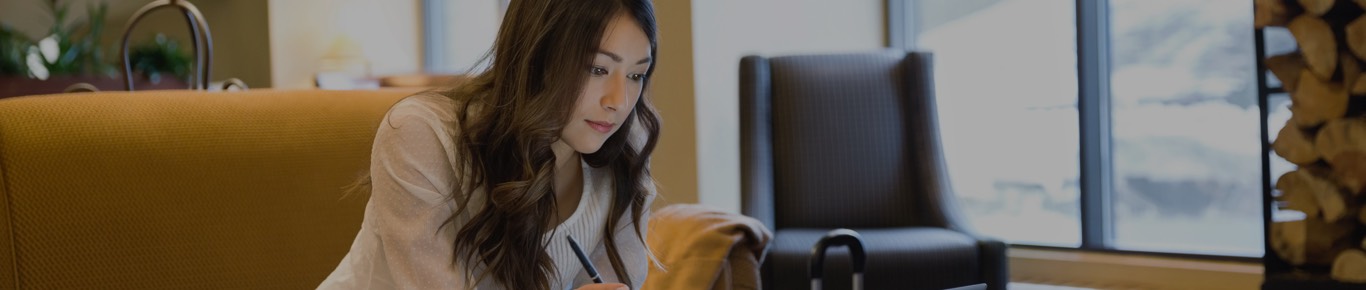 Woman sitting on couch with a pen in lobby setting.