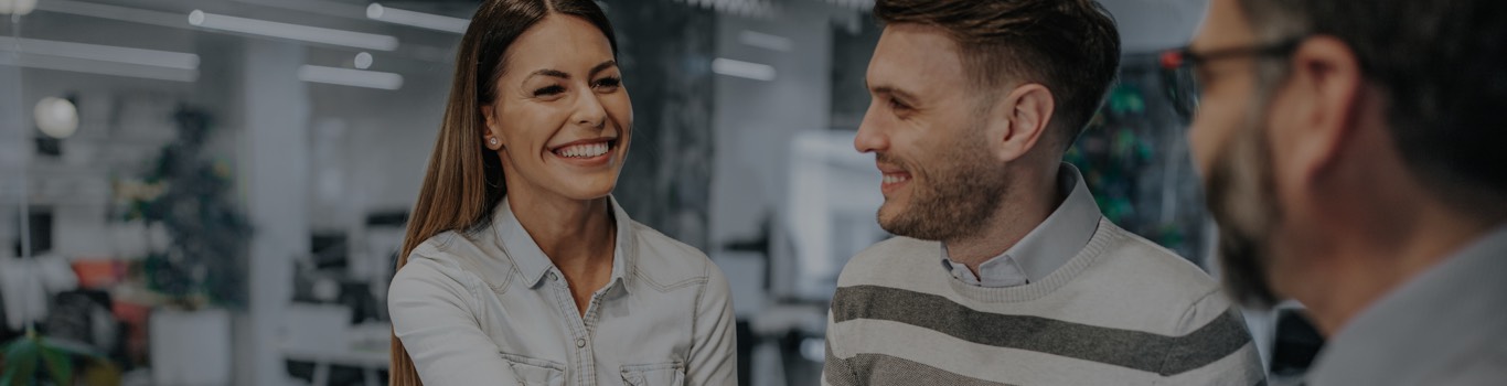 Young man and woman smiling in office talking to man in glasses.