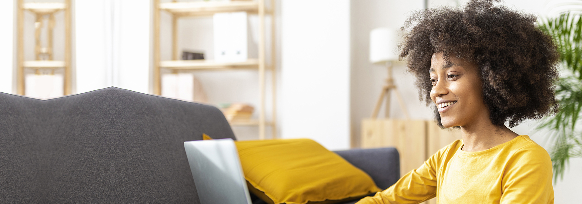Happy young woman using laptop by sofa at home