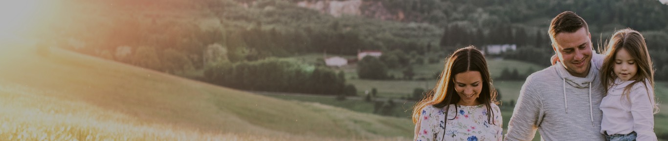 Man carrying daughter while walking with wife in countryside.