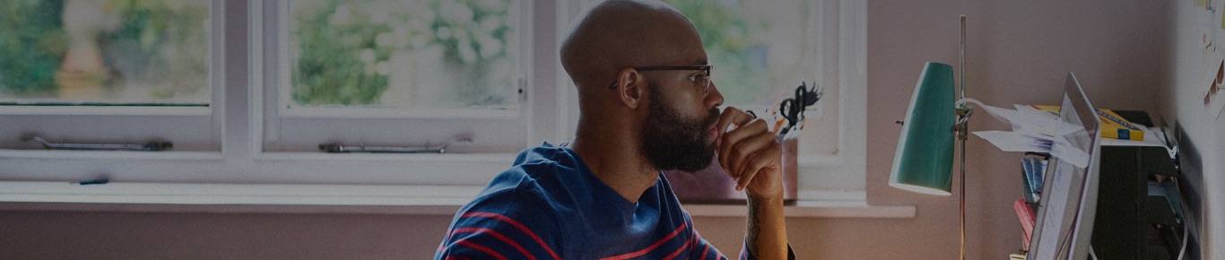 Man with beard and glasses sitting in front of laptop at home.