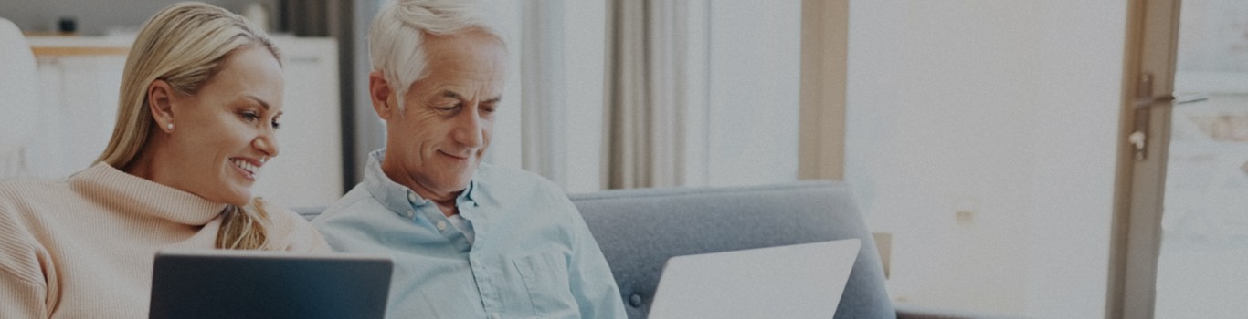 Blonde woman with laptop sitting next to an older man with laptop on couch.