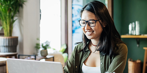 A young woman smiling while working on her laptop browsing essential health plan