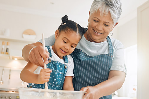 Grandmother mixing batter with help from granddaughter in the kitchen