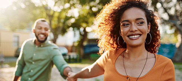 young woman smiling and holding her boyfriend's hand while walking together in a park