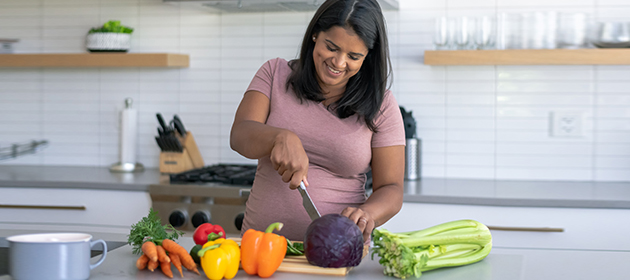 young adult woman is cutting vegetables in the kitchen and smiling