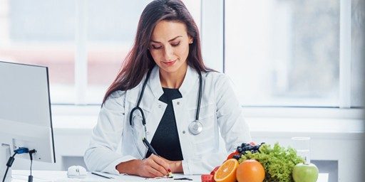 A young female registered dietitian is sitting in front of computer and making notes.