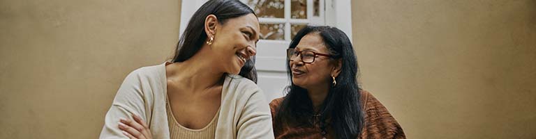 A mother and daughter sit together on the stoop, enjoying some tea and smiling