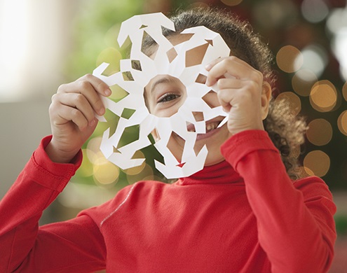 Little girl looking through a paper snowflake at the Winter Wonderland Event at a Neighborhood Care location.