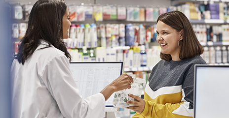 Smiling customer taking medicine from cashier at pharmacy counter.