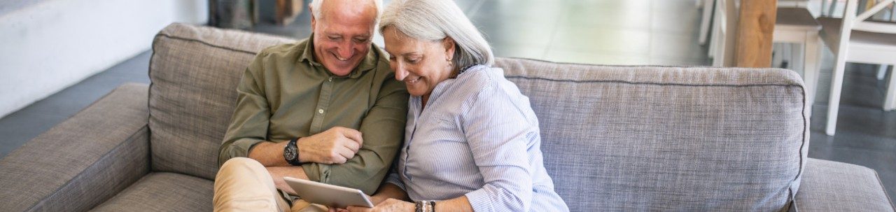 Older couple smiling and looking at a tablet device