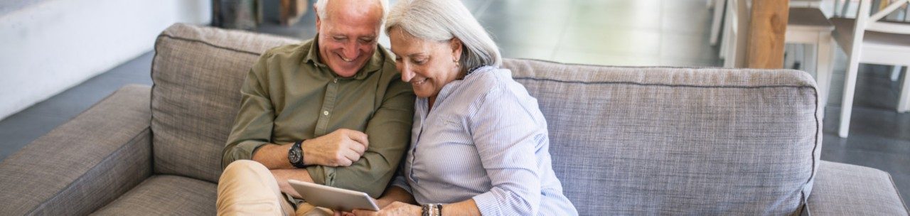 Older couple smiling and looking at a tablet device