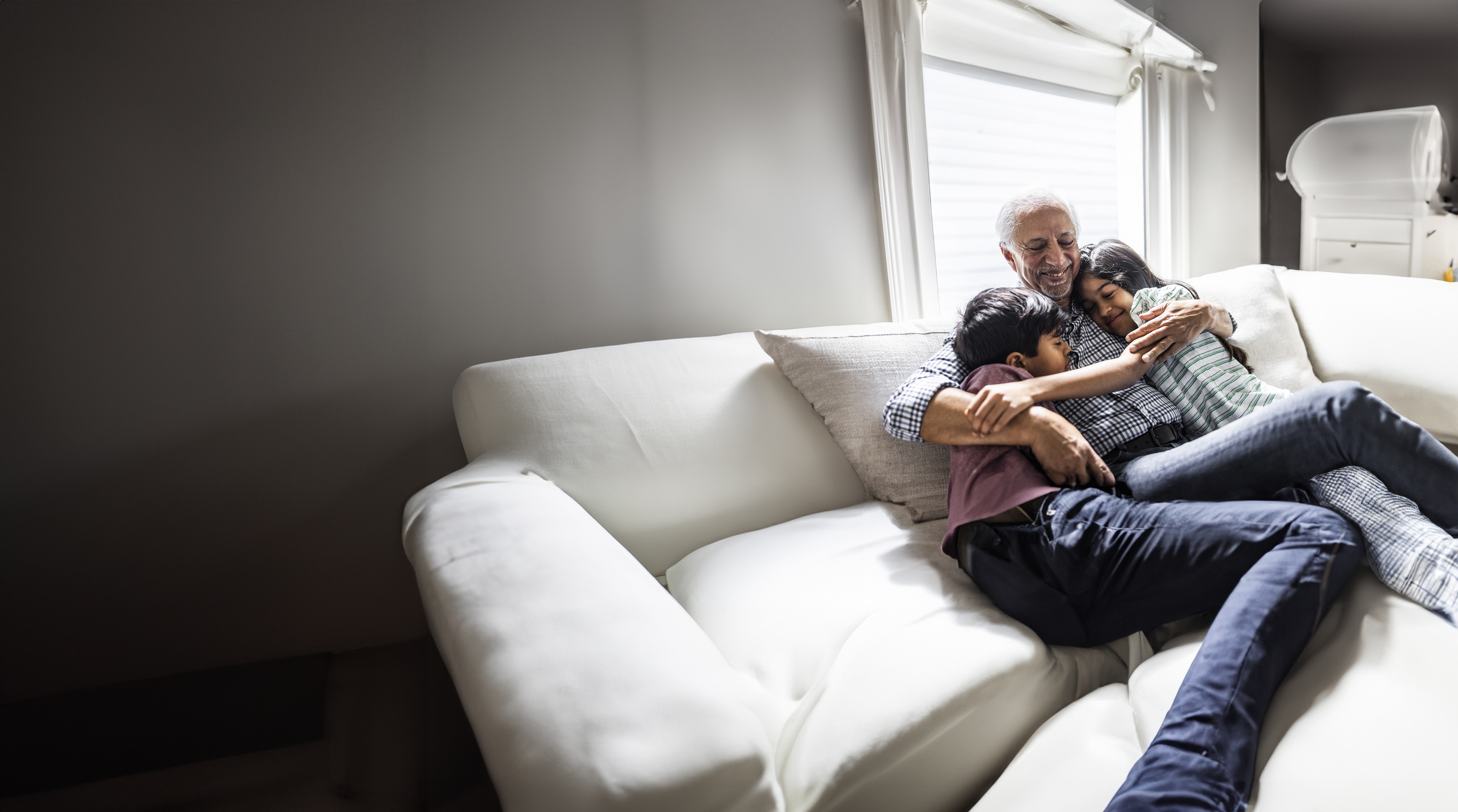 senior man huggiing grandkids on couch at home