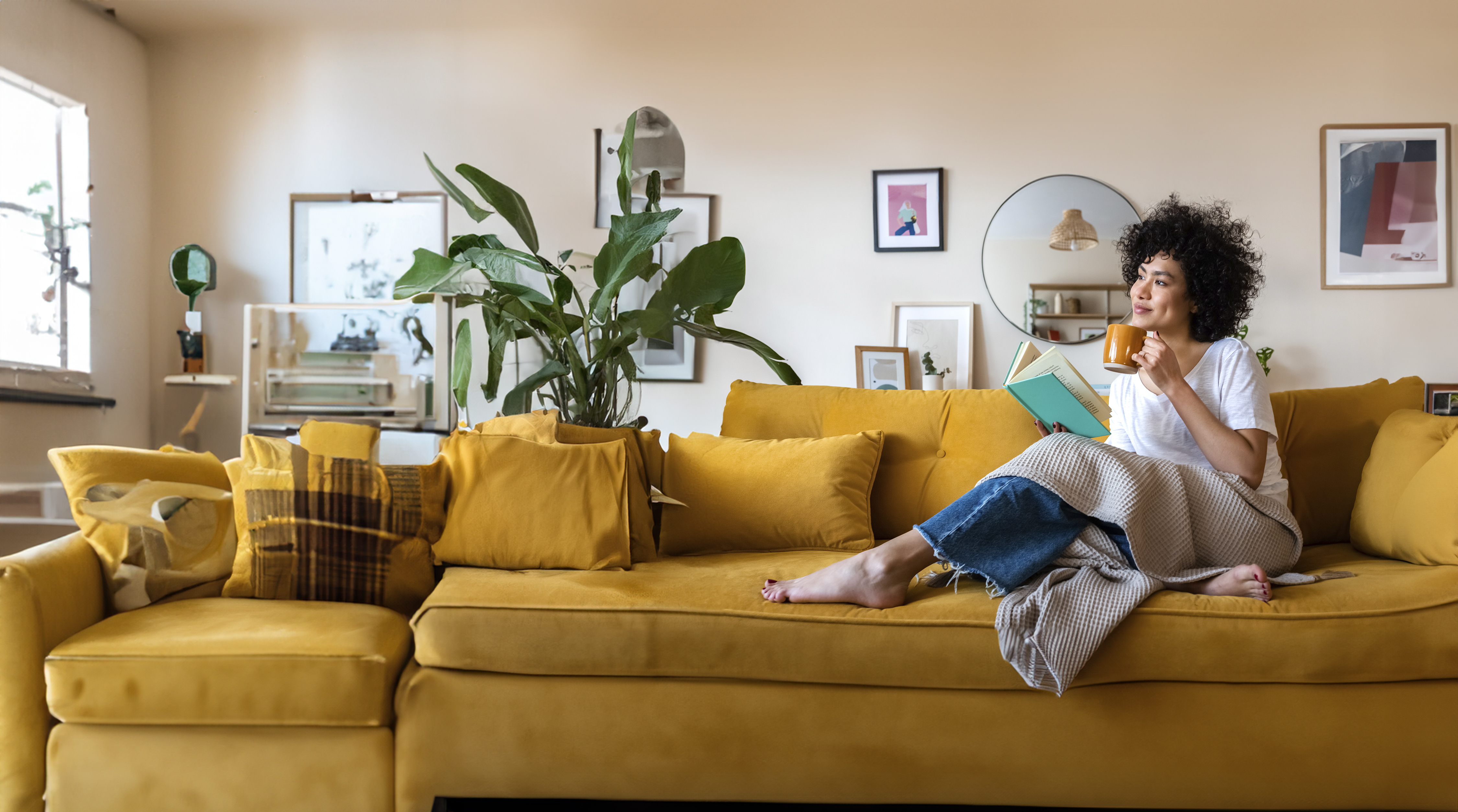 woman drinking coffee and reading a book on yellow couch 